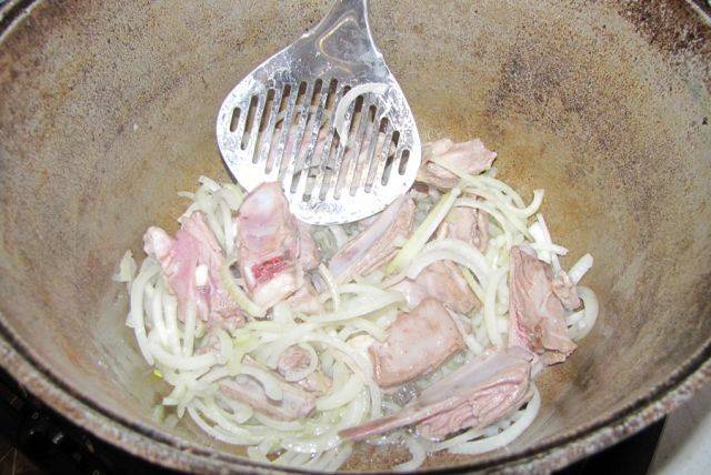Репчатый лук нарезаем полукольцами и выкладываем в казан к мясу, жарим пару минут.