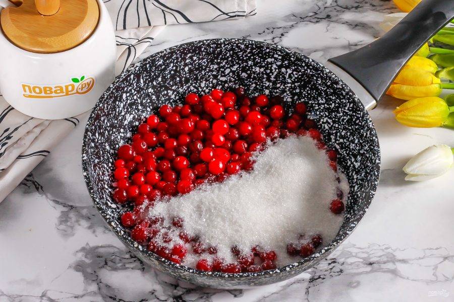 Промойте ягоды клюквы в воде и высыпьте их в сковороду или ковш с высокими бортиками. Добавьте сахар и поместите на плиту. Протомите примерно 3-5 минут.