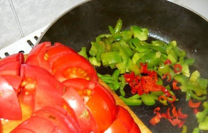 На растительном масле слегка обжариваем оба перца. Добавляем томатную пасту и порезанные помидоры, а также измельченный чеснок.