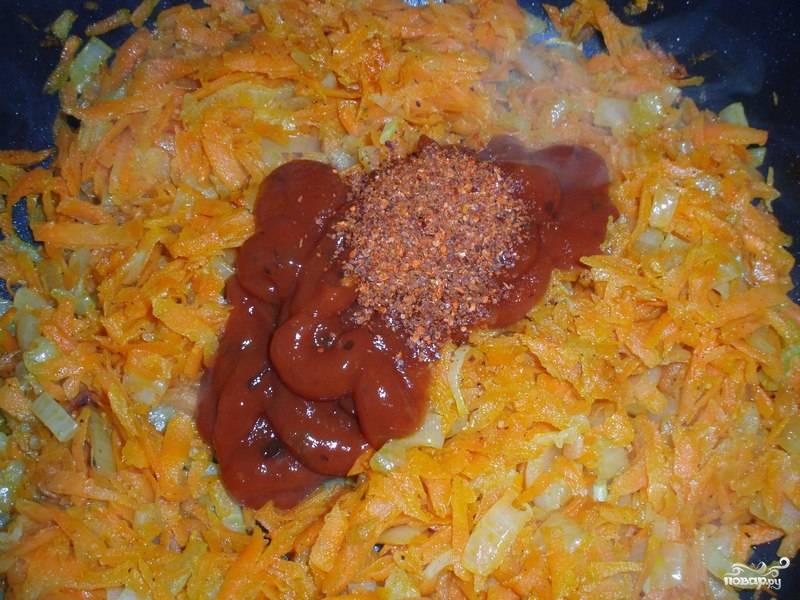 3. Выложите туда лук и морковь. Жарьте на среднем огне до мягкости. Добавьте пропущенный через пресс чеснок при желании. Когда овощи обжарились, выложите на сковороду томатный соус и специи. Использовать в рецепте приготовления тушеной капусты без масла можно также кетчуп или свежие помидоры. Все как следует перемешайте. 