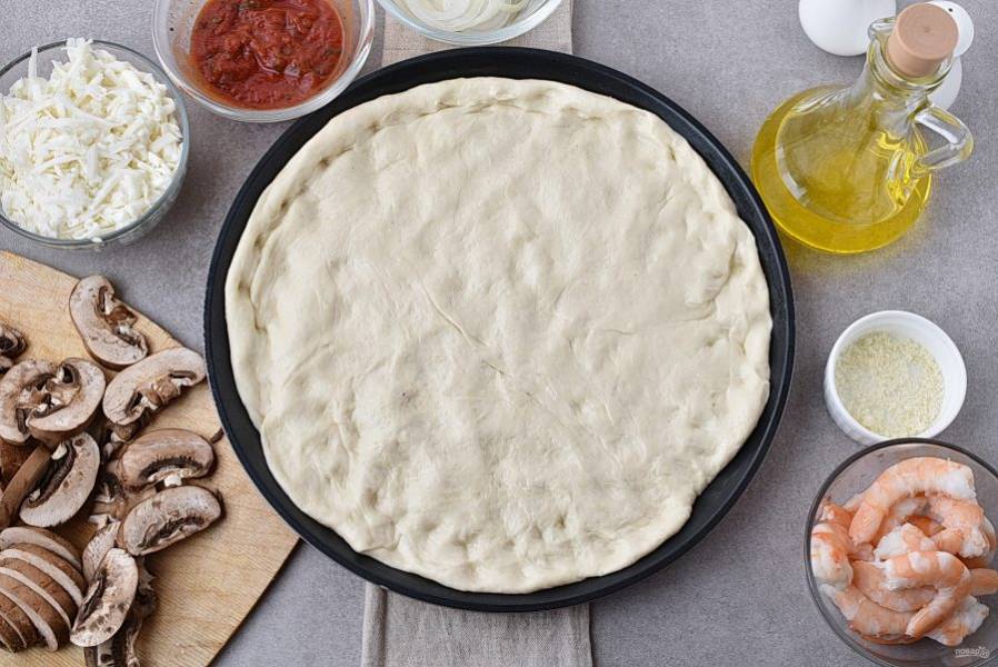 Включите духовку разогреться до 250-260 градусов. Подошедшее тесто обомните и уложите руками в форму для выпечки пиццы.