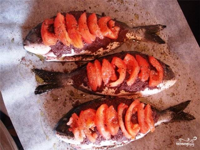 Застилаем противень бумагой для выпечки. Обмазываем рыбу пастой с сухарями и выкладываем на бумагу. Поверх рыбы укладываем дольки помидор.