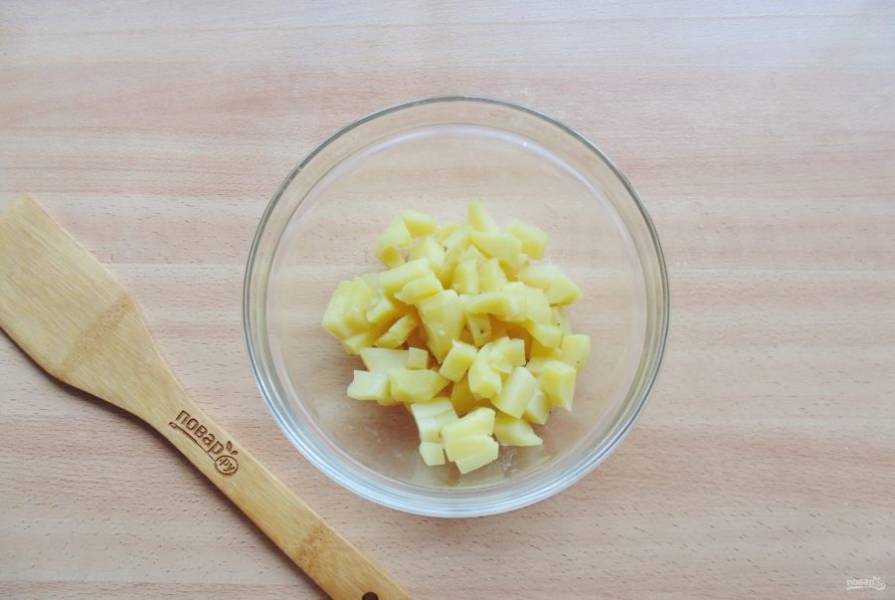 Картофель сварите в кожуре, охладите и очистите. Нарежьте мелкими кубиками и выложите в салатник.