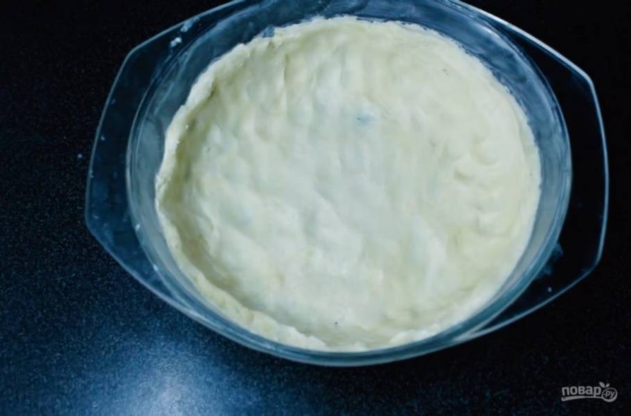 3. Форму, в которой будете выпекать пирог, смажьте сливочным маслом. Разделите тесто на две неровные части, равномерно распределите большую часть как основу пирога. Наколите дно пирога вилкой.