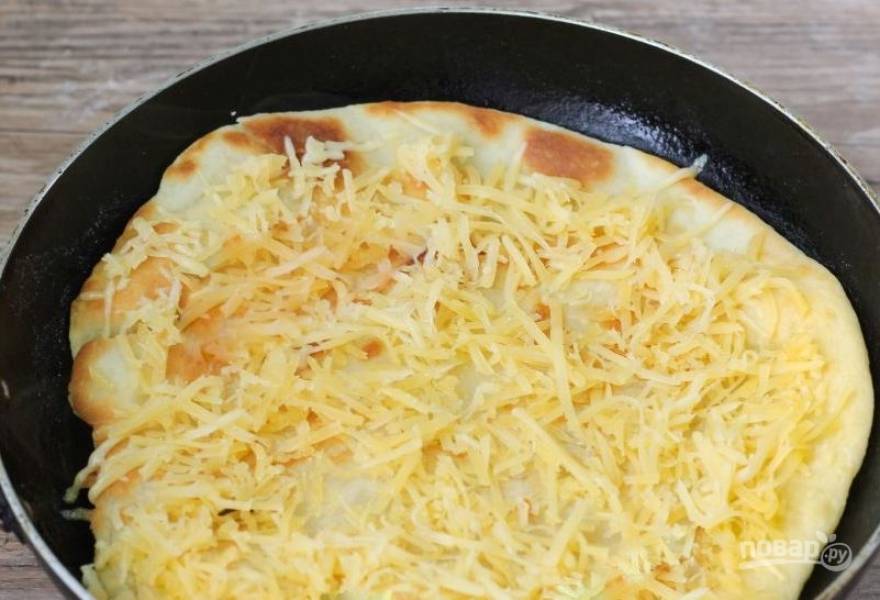 Обжаривайте на сковороде тесто с обеих сторон на среднем огне по пять минут. Оно должно стать румяным. Натрите на терке твердый сыр и выложите половину на заготовку для пиццы. 