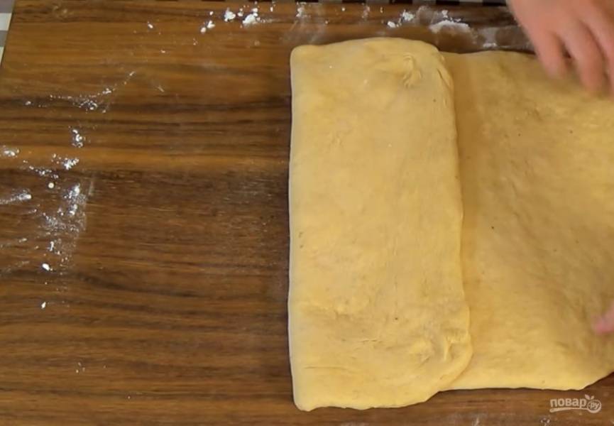3.  Постепенно добавьте просеянную муку и замесите мягкое тесто в течение 10 минут. Накройте миску пленкой и оставьте в теплом месте, чтобы тесто увеличилось вдвое. На посыпанной мукой доске сформируйте из теста прямоугольник. 