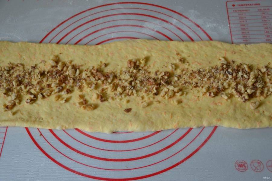 Раскатайте тесто в полоску шириной примерно 15 сантиметров, длиной 40-45, толщиной 5-7 мм. Выложите на полоску теста орехи, отступая от краев по 1,5 см. 