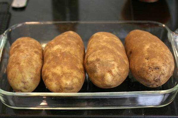 1. Вымойте крупный картофель и выложите его в форму для запекания в кожуре. Отправьте в разогретую духовку примерно на час. Затем нужно проверить готовность вилкой и при необходимости оставить в духовке еще на время. Картофель должен быть мягким, а время приготовления зависит от размера. 