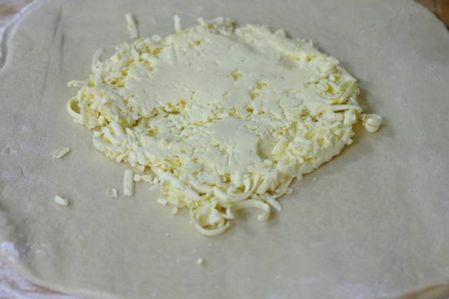 Далее раскатываем тесто не очень толстым пластом. Натираем на терке охлажденное масло и укладываем его в середину квадрата.