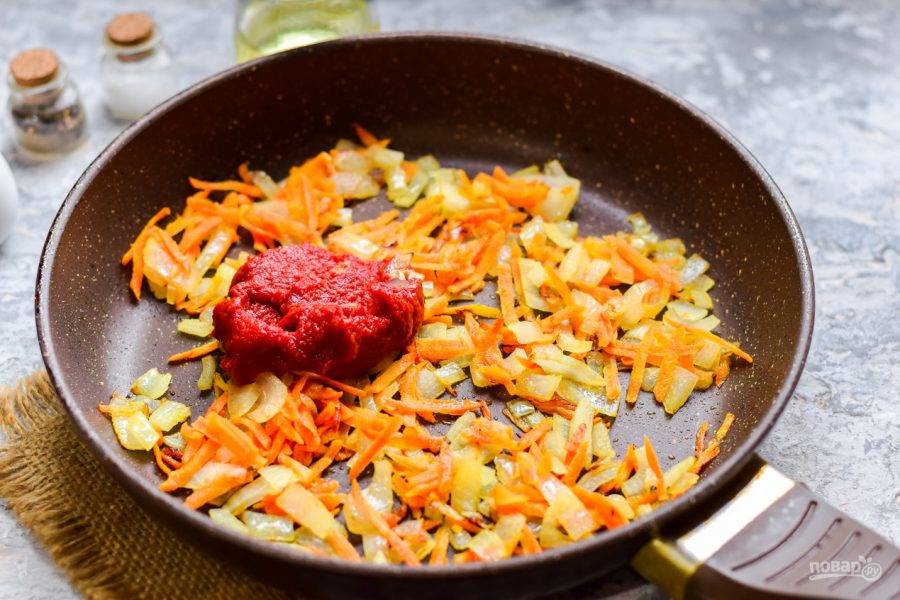 В сковороде прогрейте масло, переложите нарезанный кубиками лук и натертую средней стружкой морковь. Жарьте овощи несколько минут, добавьте пасту и воду, перемешайте.