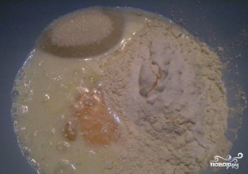 Для теста сперва разбейте в миску яйца и влейте туда кефир. Размешайте. Затем положите половину муки, сахар и соду, погашенную уксусом.