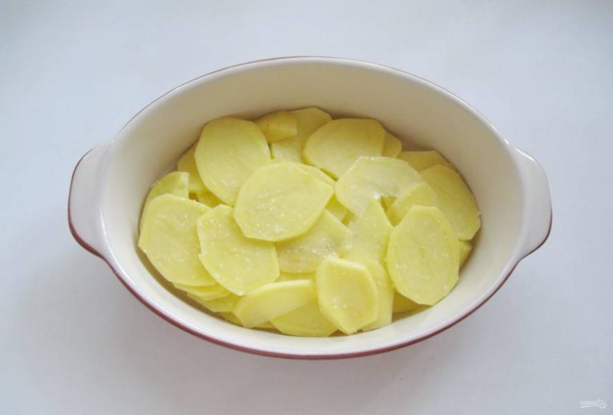 Картофель очистите, помойте и нарежьте тонкими пластинами. Выложите  в форму для запекания. Посолите по вкусу.