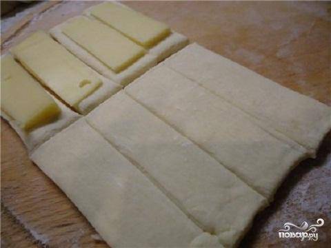 1.	Разморозить готовое слоеное тесто. Раскатать в тонкий пласт. Нарезать тесто на прямоугольники размером примерно 12 на 2 см. Сыр нарезать на тонкие полоски, размером чуть меньше прямоугольников из теста. Это нужно для того, чтобы можно было защипать края теста.