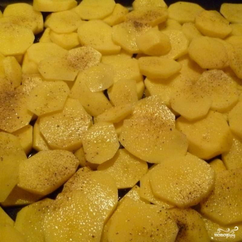 Картофель чистим, режем на тонкие пластины и укладываем на противень, смазанный маслом.