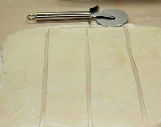 Раскатайте из теста тонкий прямоугольный пласт, чтобы не липло – посыпьте немного мукой. Затем нарежьте тесто полосками. Толщина пласта должны быть около 4 мм., а ширина полоски 8-10 см. 
