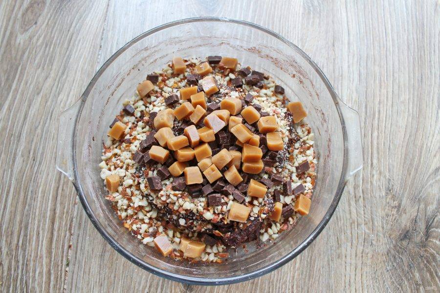 Мягкие ириски порежьте на кусочки и добавьте в миску с тестом, орехами и шоколадом.