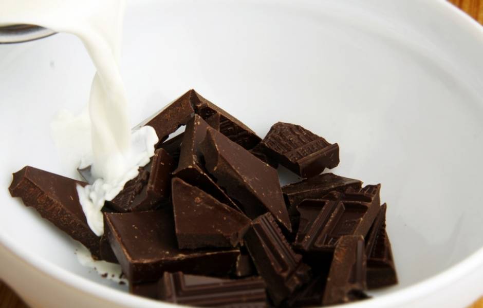 Пора делать начинку. Разломайте шоколад кусочками, переложите его в миску и залейте горячими сливками. Быстро и тщательно перемешайте до однородности. 