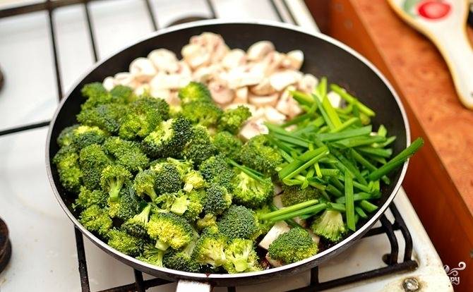 На сковороду добавить нарезанные и отваренные грибы и брокколи, а также крупно порезанный зеленый лук.