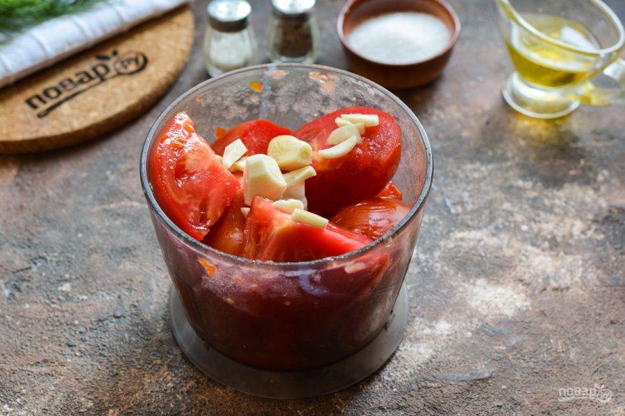 Порционно перекладывайте томаты в чашу блендера. Очистите чеснок и добавьте к помидорам.