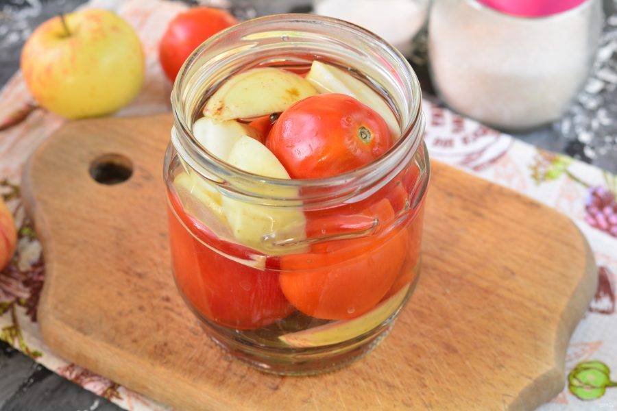 Залейте помидоры горячим маринадом. Оставьте на 10 минут, прикрыв крышкой. Затем маринад слейте обратно в миску или кастрюлю, снова закипятите и повторно залейте помидоры с яблоками горячим маринадом.
