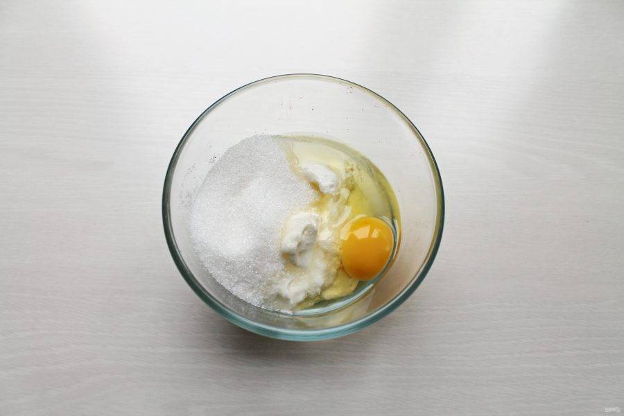 Для заливки в миску выложите сметану, добавьте оставшийся сахар и разбейте второе яйцо. Все хорошенько взбейте до однородной массы.