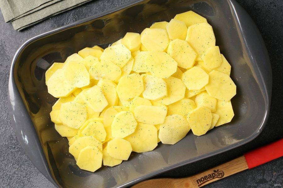 Жаропрочную форму смажьте маслом. Картофель нарежьте тонкими кружочками и выложите в 2-3 слоя. Каждый слой посолите и поперчите.