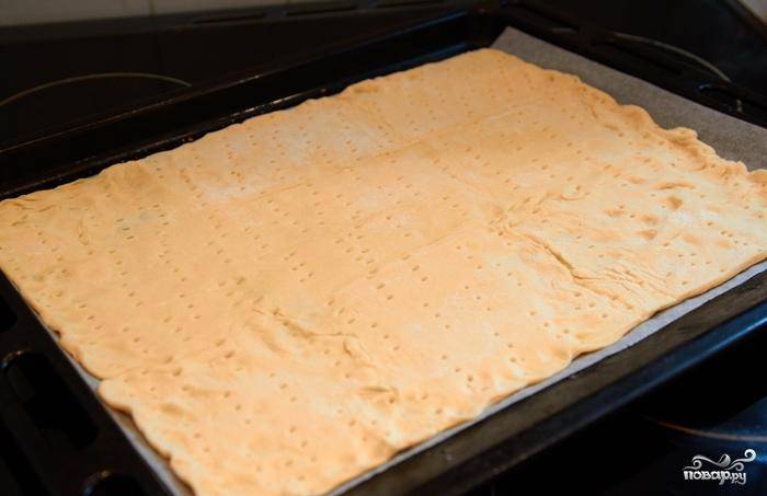 Готовое слоеное тесто раскатываем в пласт и выкладываем на слегка смазанный маслом противень. Накалываем тесто вилочкой - как на фото. Это делается для того, чтобы тесто не вздувалось после запекания.
