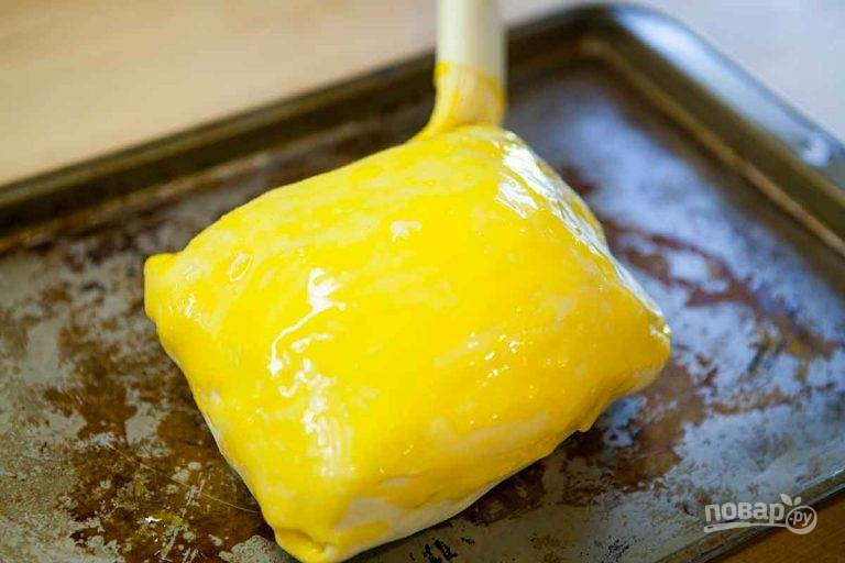 9. Выложите мясо в тесте швом вниз на противень и смажьте желтком.