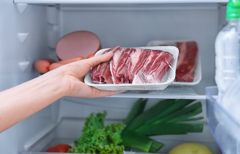 Женщина кладет мясо в холодильник